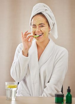 Shot of a young woman eating a cucumber while doing a facial beauty treatment at home.