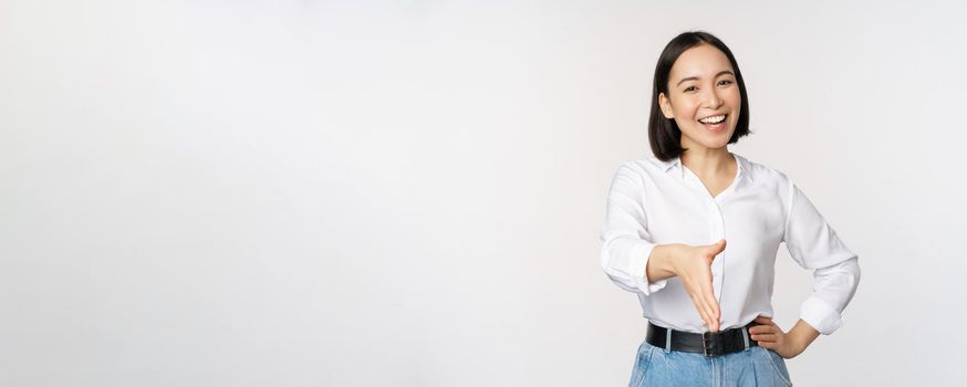 Image of confident asian woman smiling, extend hand for handshake greeting gesture, saying hello, standing over white background