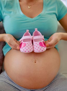 Cute shoes for my precious little princess. Closeup shot of a pregnant woman holding a pair of pink baby shoes against her belly at home.