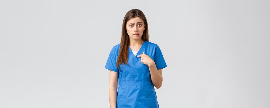 Healthcare workers, prevent virus, insurance and medicine concept. Nervous and confused female nurse, doctor in blue scrubs, biting lip anxious pointing herself, being confused waiting answer