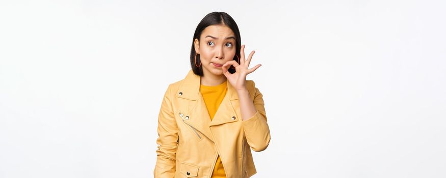 Image of young asian woman seal lips, silence gesture, zipping her mouth with promise, standing over white background