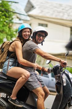 Adventure awaits. Portrait of two happy backpackers riding a motorcycle through a foreign city.