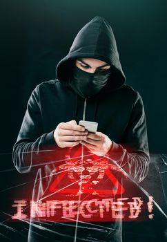 Not even your smartphone is safe. Shot of a computer hacker using a smartphone while standing against a dark background.
