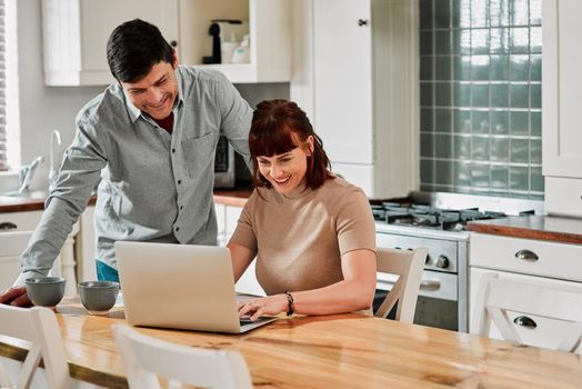 Hows your online course going, babe. Shot of a woman using a laptop with her husband standing beside her.