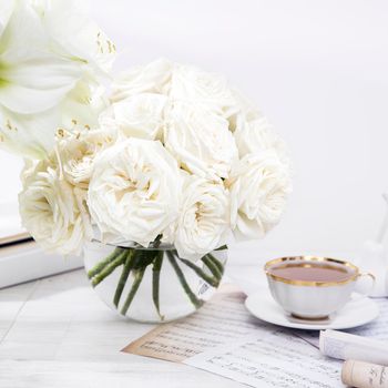 White roses, lily, in round vases with two cups of coffee on the table for a special occasion as a kitchen decoration.