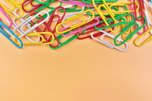Multicolored Paperclips Isolated on a Cheerful Orange Beige Background with Copy Space on Bottom