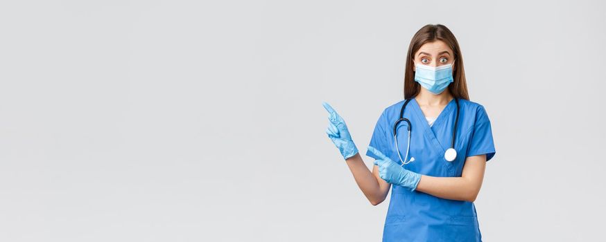 Covid-19, preventing virus, health, healthcare workers and quarantine concept. Interested and questioned female doctor, nurse in blue scrubs and medical mask, asking question pointing left