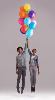 Lets fly away. Studio shot of a young couple holding a bunch of balloons as they float away.
