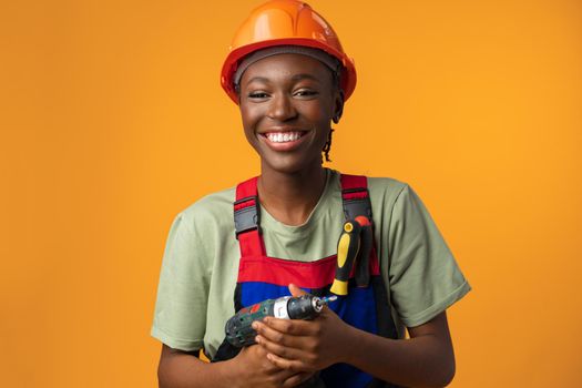 Smiling young african american woman in hardhat holding screwdriver tool in studio