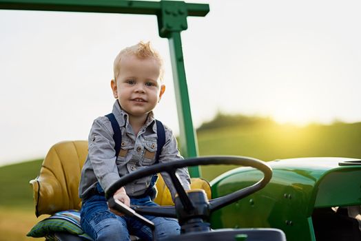 Growing up with good old fashioned farming values. Portrait of an adorable little boy riding a tractor on a farm.