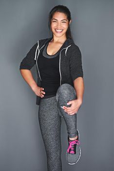 Shot of a fit young woman stretching her legs against a gray background.