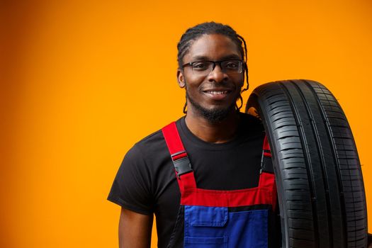African american car service worker with car tyre against yellow background