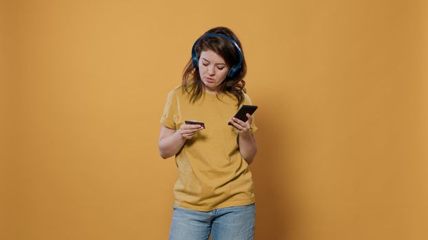 Woman holding smartphone typing credit card details doing online shopping while listening to music