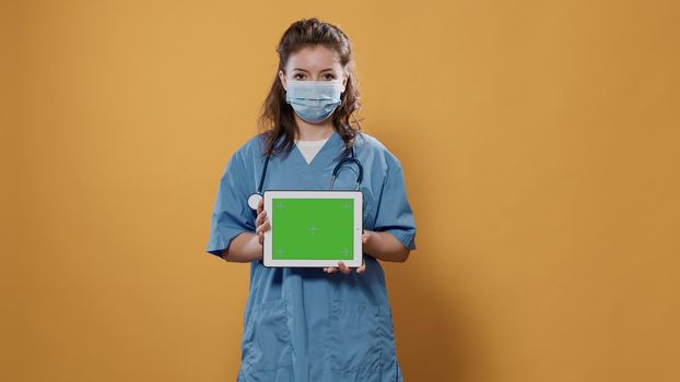 Portrait of woman doctor holding tablet computer with green screen wearing hospital uniform and covid protection mask