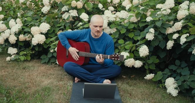 Man in with guitar in park nature is streaming online podcast using gadgets