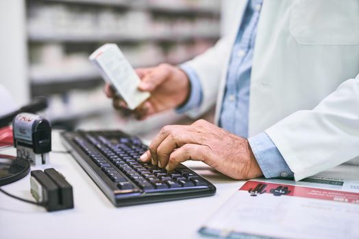 This will fix you up. Shot of a unrecognizable pharmacist typing on a computer keyboard while holding a medication subscription.