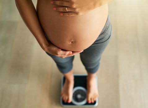 Pregnancy by the pounds. Cropped high angle shot of a pregnant woman weighing herself on a scale.