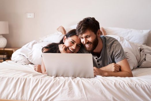 Shot of a happy young couple using a laptop while relaxing on the bed at home.