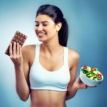 Live your healthy life. Shot of an attractive young woman choosing between a salad and a chocolate.