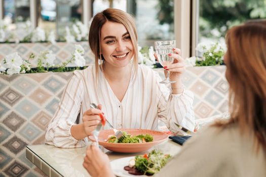 Cheerful Young Woman Having Lunch with Her Female Friend in the Restaurant