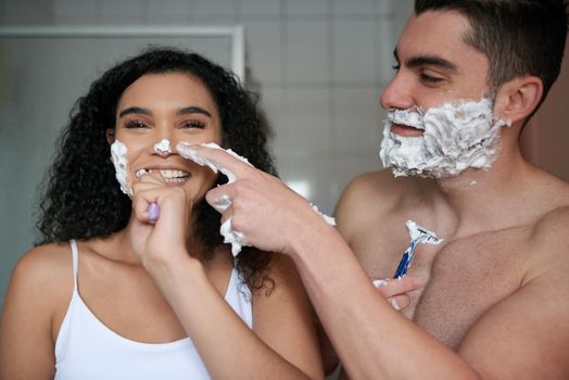 Their morning routine is full of fun. Portrait of an attractive young woman brushing her teeth while her boyfriend shaves in the bathroom.