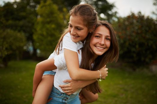 Im her biggest supporter. Cropped portrait of a young girl giving her younger sister a piggyback ride outdoors.