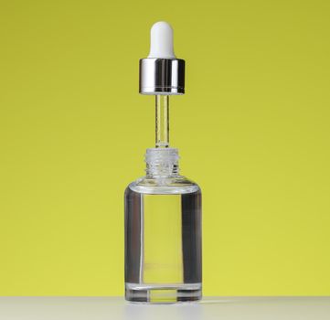 White bottle of cosmetic oil with a pipette, green background