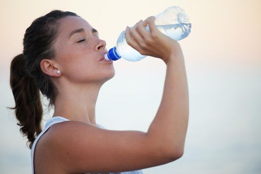 Drink more water, your body will thank you for it. Shot of a sporty young woman drinking water while out for a run.