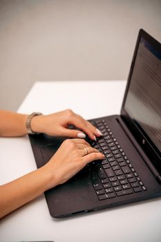 European professional woman sitting with laptop at home office desk, positive woman studying while working on PC. She is wearing a red plaid shirt and jeans.