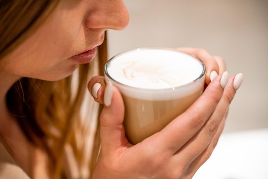 Close-up of beautiful female hands holding a large white cup of cappuccino. A woman is sitting in a cafe.