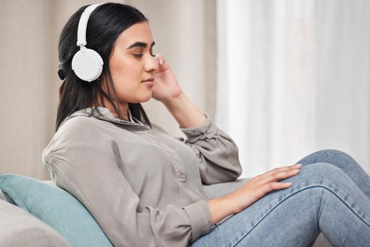 Music calms me. Shot of a young woman listening to music wearing headphones at home.