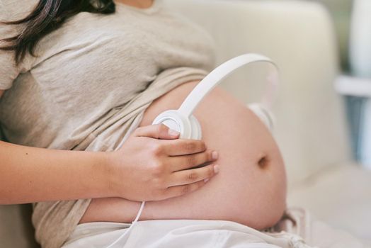Enhance the stimulation of your unborn babys growing brain. Shot of a woman wearing headphones over her pregnant belly.