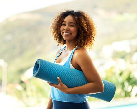 Portrait of an attractive young woman standing outside with her yoga mat.