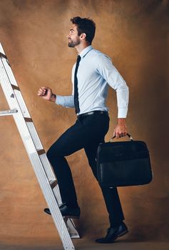 Up is the only option. Studio shot of a handsome young businessman climbing a ladder against a brown background.