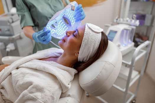Woman getting cosmetic procedure with LED facial mask. Photon therapy