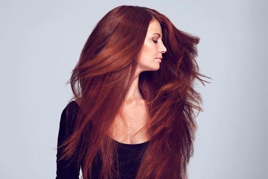 Lovely luscious locks. Studio shot of a young woman with beautiful red hair posing against a gray background.