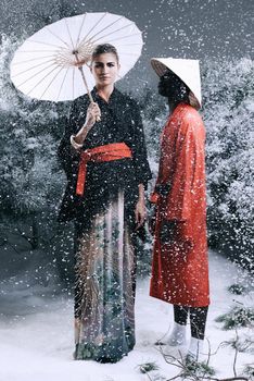Fashion shot of a man and woman wearing oriental-style clothing in a snowy forest.