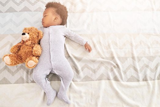 High angle shot of a little baby boy sleeping on a bed with a teddy bear.