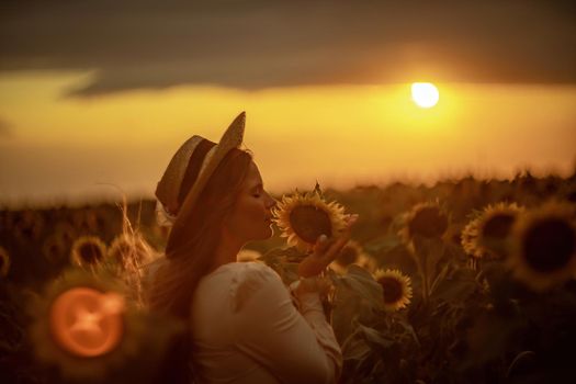 Beautiful middle aged woman looks good in a hat enjoying nature in a field of sunflowers at sunset. Summer. Attractive brunette with long healthy hair.