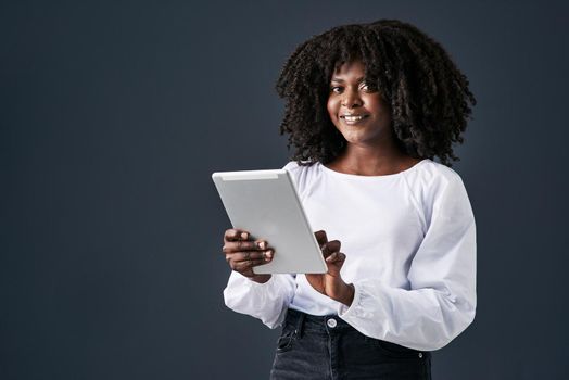 I leave never leave the house without my tech. Shot of a young businesswoman using a digital tablet against a studio background.