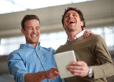 Take time out for a good old laugh. Male coworkers laughing out loud about something humorous on a digital tablet in their office.