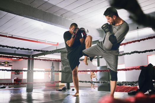 Using some kicks to mix it up. Shot of two young male boxers facing each other in a training sparing match inside of a boxing ring at a gym during the day.