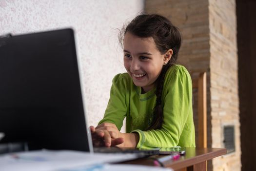 Smiling little Caucasian girl in headphones have video call distant class with teacher using laptop, happy small child wave greeting with tutor, study online on computer, homeschooling concept