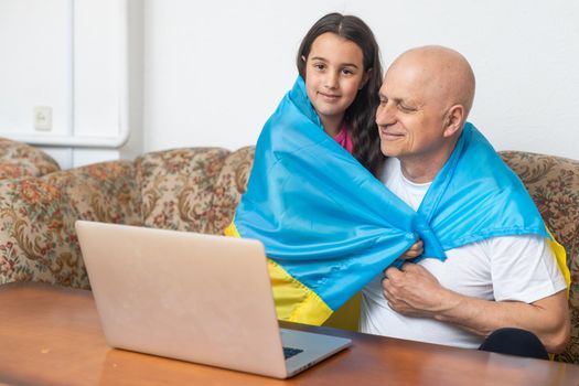 Grandfather and granddaughter with laptop and flag of Ukraine