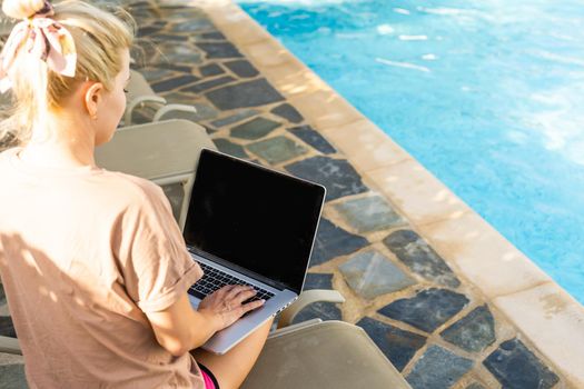 Excited woman relaxing on sun lounger with laptop near the pool