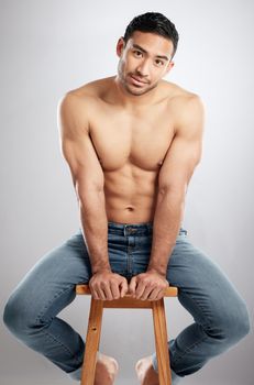 Desire strong enough to see. Studio shot of a handsome young man showing off his muscular body while sitting on a chair against a grey background.