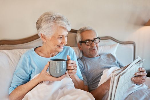 We still like the good old fashioned newspaper. Cropped shot of a senior man reading a newspaper in bed while his wife drinks a cup of coffee.