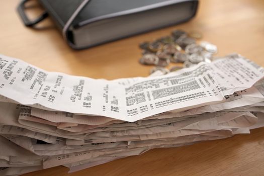 A stack of receipts in the Foreground with Coins and Accordion Folder Organizer in Background