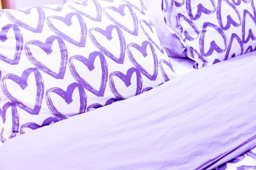 cozy set of purple pillows with hearts and textures textiles.Comfortable pillow on sofa decoration.Interior with bed with white bed linen and colored pillows.