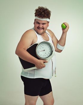 Lets do this. Cropped shot of an overweight man holding a apple,scale and measuring tape.